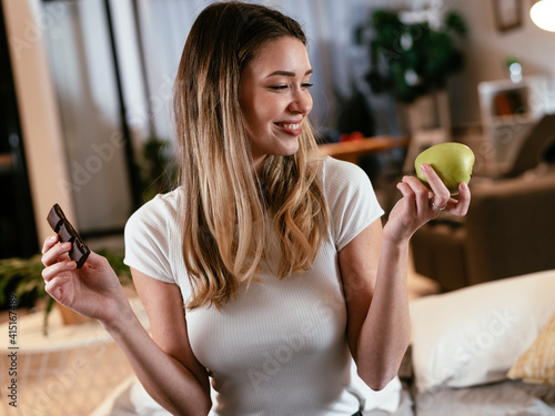 Young woman holding an apple and a chocolate bar. Fit woman choosing between eating healthy or chocolate.. photo