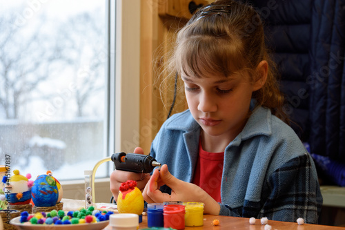 A girl glues a decorative element to crafts with a glue gun photo