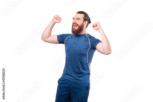 Joyful young bearded fitness man celebrating success over white background.