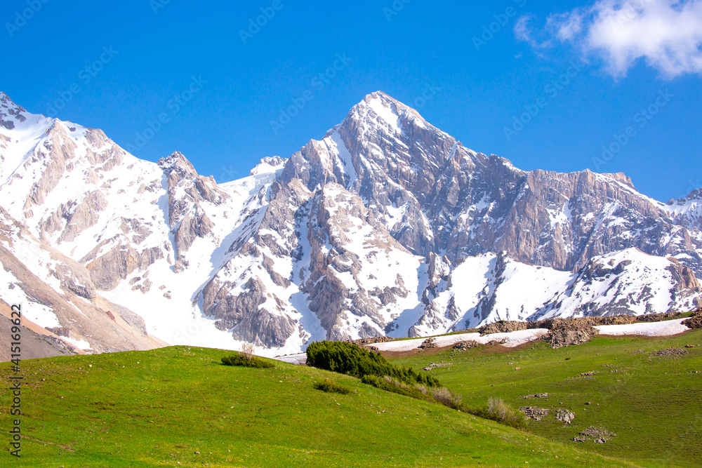 A beautiful natural mountain landscape in spring with green grass, in a valley with a blue sky on top - this is the concept of a hike in mountain tourism and travel rock cliffs