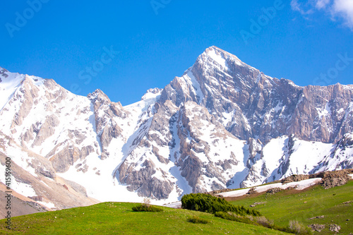 A beautiful natural mountain landscape in spring with green grass, in a valley with a blue sky on top - this is the concept of a hike in mountain tourism and travel rock cliffs