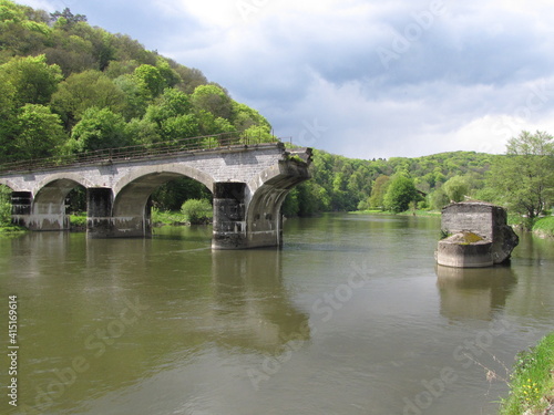 the famous bombed bridge over river semois between green hills with a forest with pine trees in springtime in bohan in the belgian ardennes photo