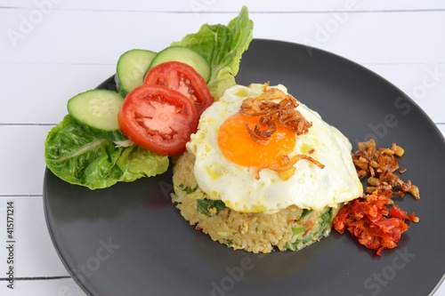 Nasi goreng or Indonesian fried rice with egg garnished with  lettuce, fresh cucumber slices , slice tomato, sunny side up, fried egg, sambal and fried onion