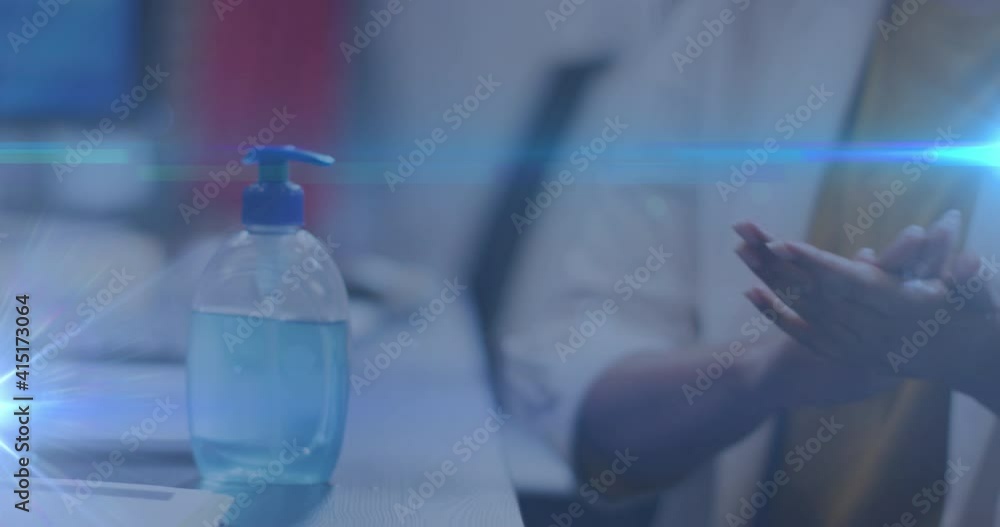 Blue light trails against mid section of woman using hands sanitizer at office Blue light trails against mid section of woman using hands sanitizer at office