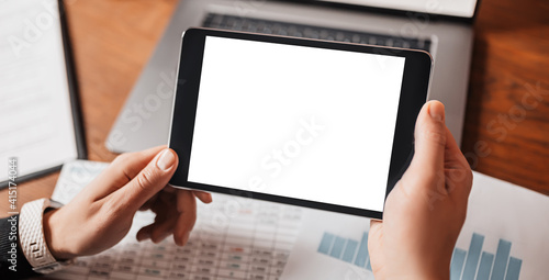 Male hands holding tablet with blank background at workplace. Businessman working at desk with documents