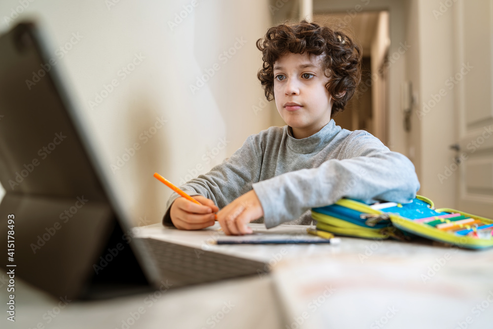 Remote schooling in coronavirus new normal time: a schoolboy is making online lessons thru the internet with a modern tablet Remote schooling in coronavirus new normal time: a schoolboy is making online lessons thru the internet with a modern tablet