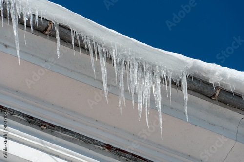 The roofs of the buildings are covered with snow and ice after a big snowfall. Huge icicles hang from the facades of buildings. The fall of icicles carries a danger to people's lives.