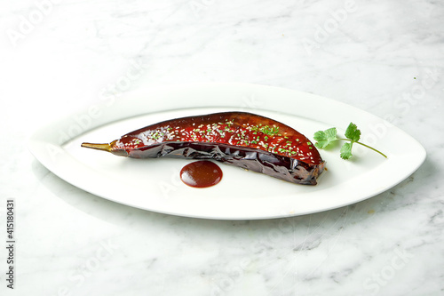 Baked eggplant in josper with miso sauce, cilantro, nuts and sesame seeds. Miso eggplant in a white plate on a marble background. View from above photo