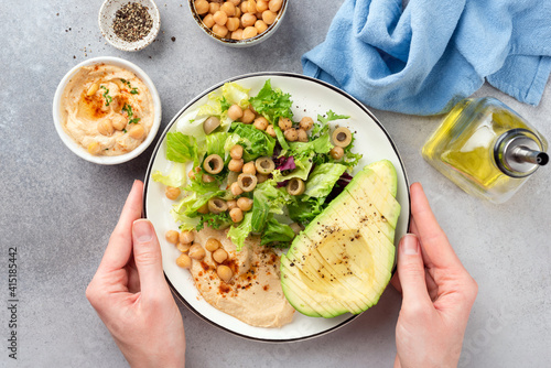 Female hands holding salad buddha bowl with avocado, chickpea hummus and greens. Top view. Clean eating, dieting concept © Vladislav Noseek