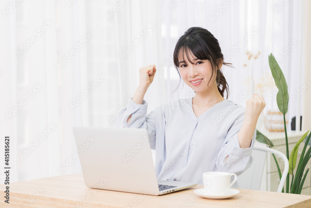 部屋でノートパソコンを使いながらガッツポーズをする若い女性 部屋でノートパソコンを使いながらガッツポーズをする若い女性
