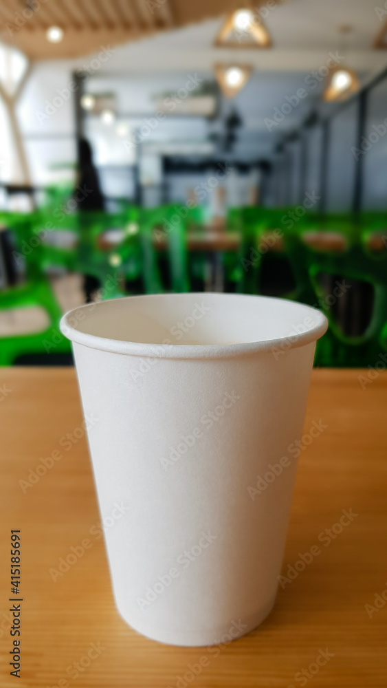 Paper white coffee cup disposable to take or go, on the wooden table of the coffee shop or dining room, place for a designer layout. Hot coffee cup in a cafe.