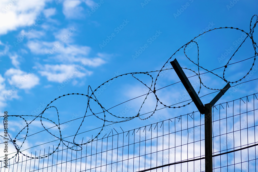 Silhouette of a metal fence with barbed wire from above against the blue sky. Silhouette of a metal fence with barbed wire from above against the blue sky.