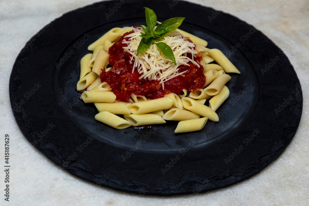 Penne pasta with red sauce and parmesan cheese on a black plate.  Stone or concrete background