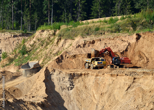 Excavator load the sand to the heavy mining truck in the open-pit. Heavy machinery working in the mining quarry. Digging and excavation operations.