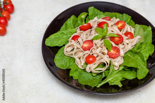 Wholemeal pasta with green leaves of arugula and Cherry tomato on black plate and white marble background