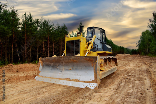 Dozer during clearing forest for construction new road. Bulldozer at forestry work on sunset background. Earth-moving equipment at road work, land clearing, grading, pool excavation, utility trenching