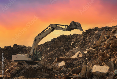 Recycling concrete and construction waste from demolition. Excavator at landfill of the disposa. Reuse of building rubble. Backhoe dig gravel at mining quarry on sunset background. Concrete debris