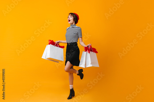 Full length view of excited slim woman with store bags. Studio shot of fashionable shopaholic girl.