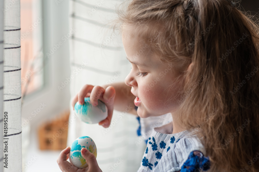 A cute little girl with long curly hair holds Easter eggs in her hands. Portrait. Close-up A cute little girl with long curly hair holds Easter eggs in her hands. Portrait. Close-up