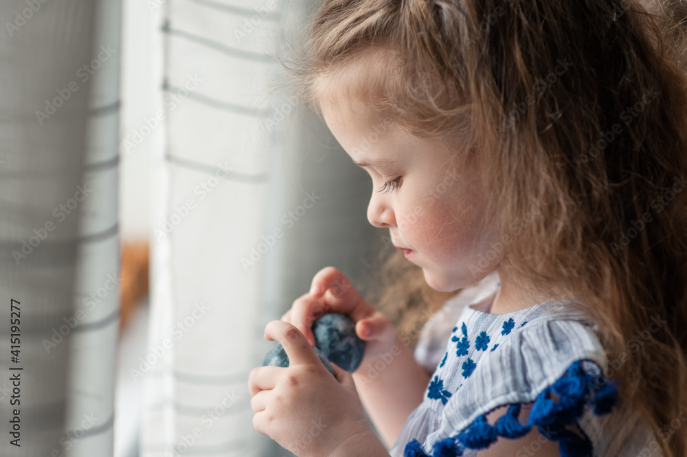 A cute little girl with long curly hair holds Easter eggs in her hands. Portrait. Close-up A cute little girl with long curly hair holds Easter eggs in her hands. Portrait. Close-up