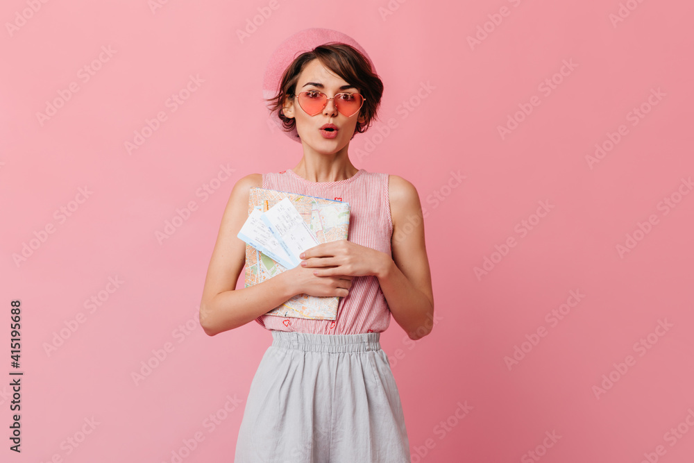 Amazed glamorous woman waiting for travel. Studio shot of short-haired lady with tickets isolated on pink background. Amazed glamorous woman waiting for travel. Studio shot of short-haired lady with tickets isolated on pink background.