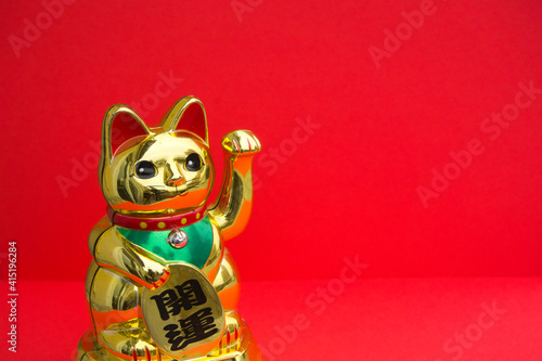 Maneki-neko. Japanese Chinese cat of fortune and luck on a red background with copy space