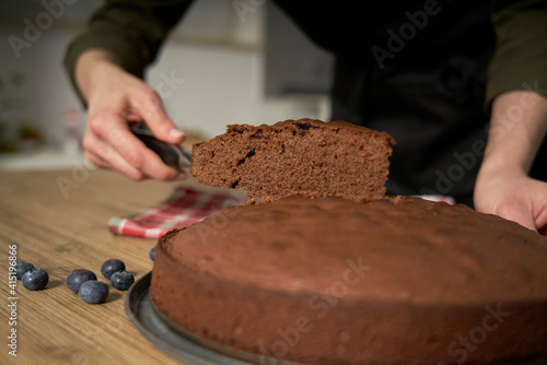 Woman with a passion for cooking cuts a slice of handmade chocolate cake in her home kitchen.