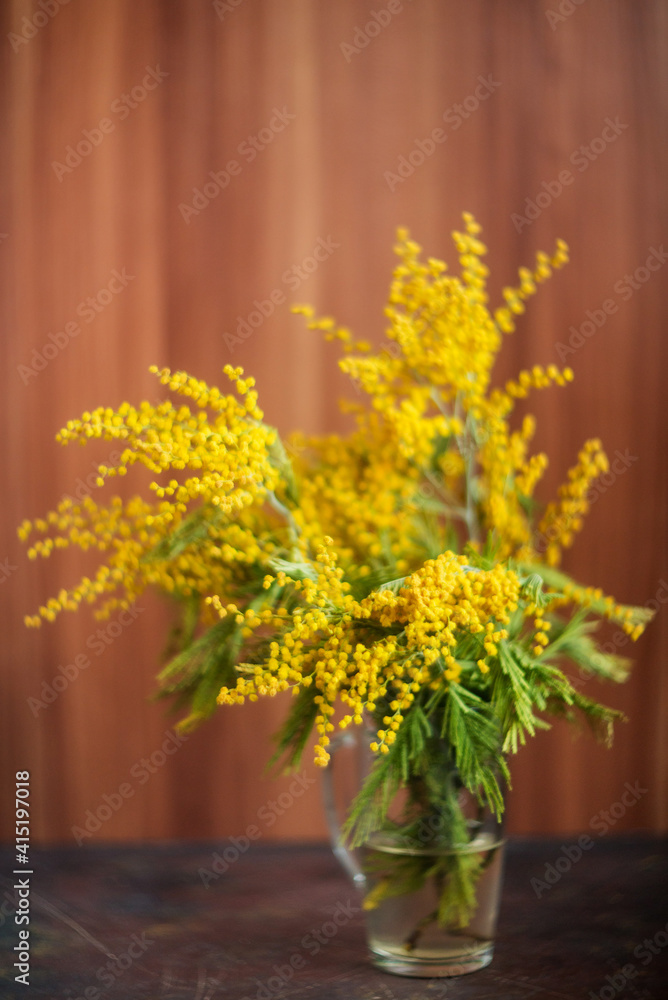 Bouquet of yellow mimosa in a vase on a wooden background