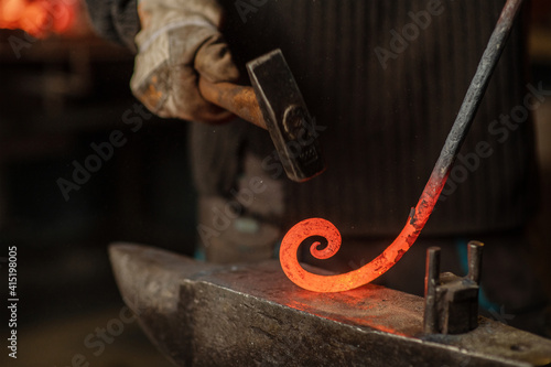 The blacksmith hits the red-hot workpiece in the forge with a hammer and glowing sparks fly in all directions