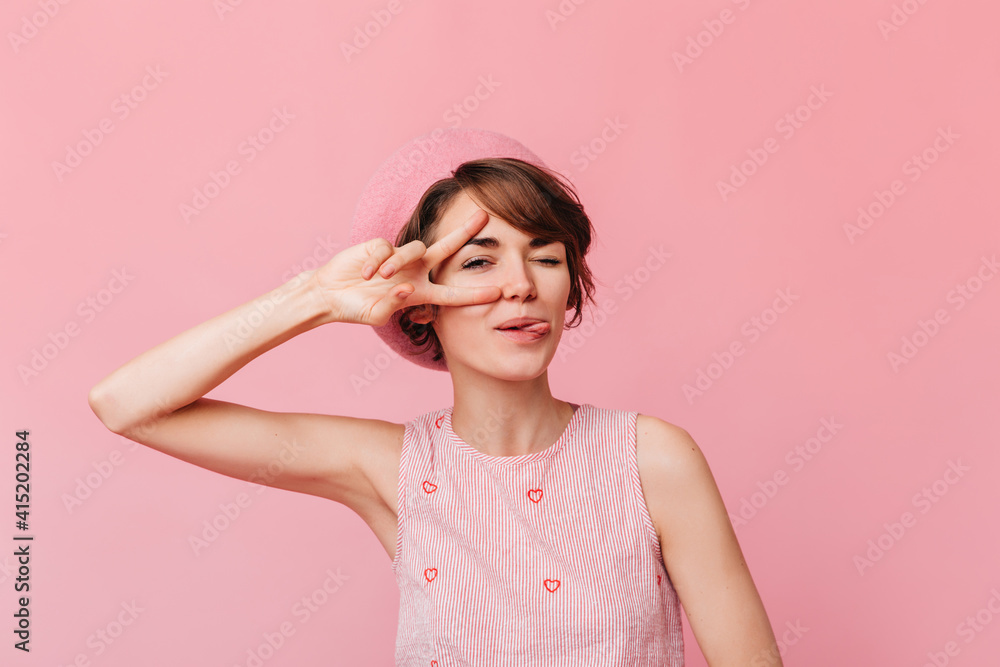 Jocund caucasian girl showing peace sign. Studio shot of attarctive french woman gesturing on pink background. Jocund caucasian girl showing peace sign. Studio shot of attarctive french woman gesturing on pink background.