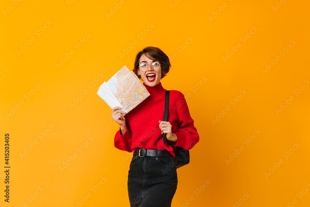 Excited female traveller in red sweater standing on yellow background. Studio shot of woman with map. Excited female traveller in red sweater standing on yellow background. Studio shot of woman with map.