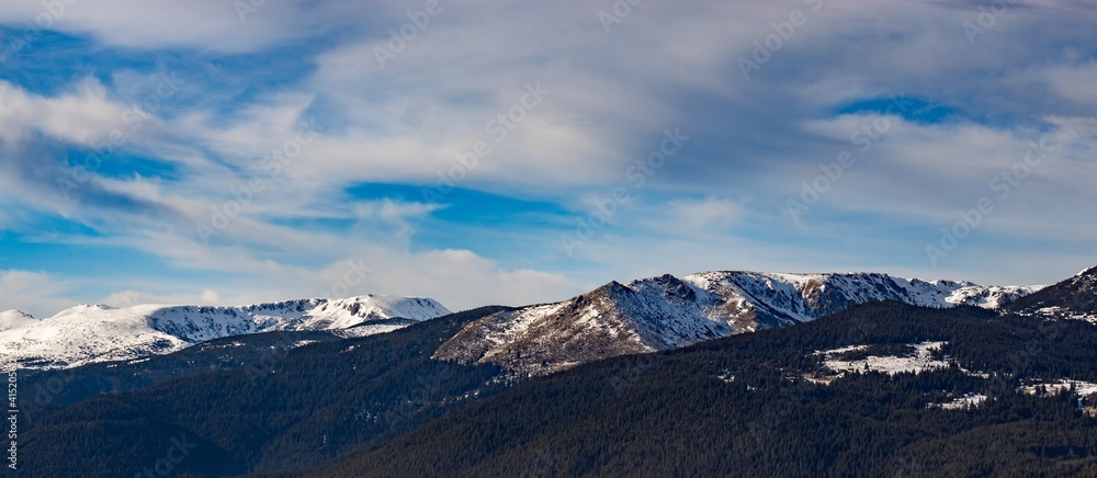 Beautiful winter panoramic natural mountain landscape. Attractive snowy peaks of Rila Mountains, Bulgaria. White clouds in dynamic blue sky, perfect conditions for tourism recreation and winter sports Beautiful winter panoramic natural mountain landscape. Attractive snowy peaks of Rila Mountains, Bulgaria. White clouds in dynamic blue sky, perfect conditions for tourism recreation and winter sports