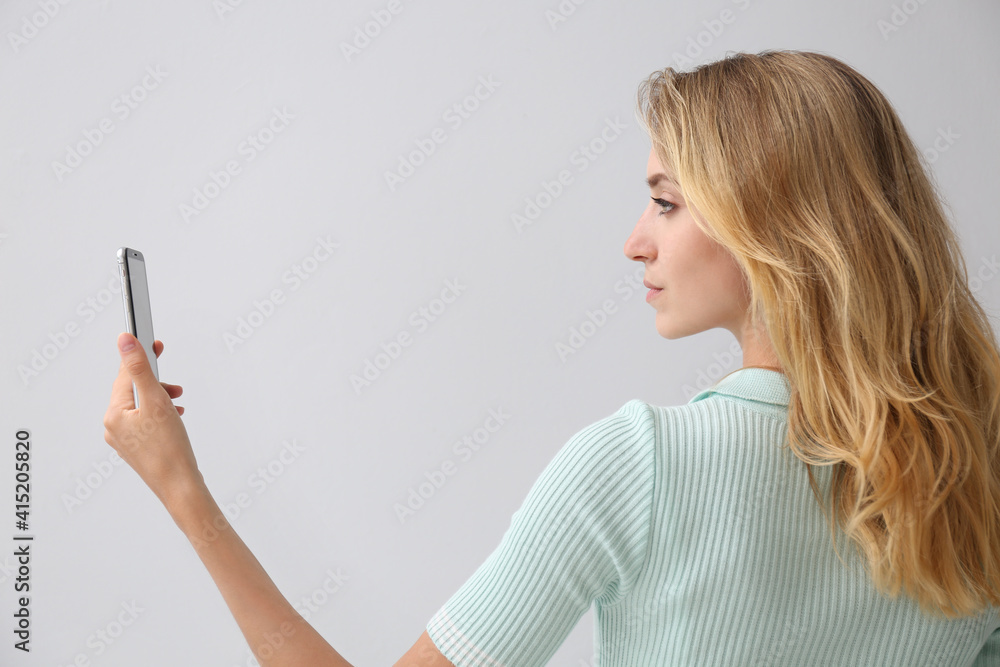 Young woman unlocking smartphone with facial scanner on grey background. Biometric verification Young woman unlocking smartphone with facial scanner on grey background. Biometric verification