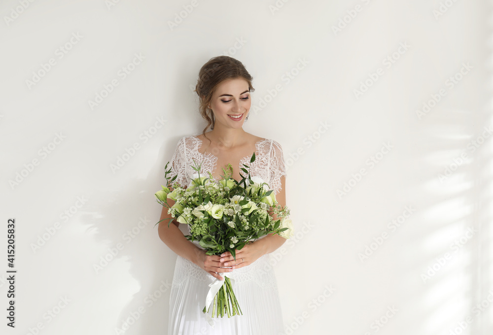 Young bride wearing wedding dress with beautiful bouquet on light background Young bride wearing wedding dress with beautiful bouquet on light background