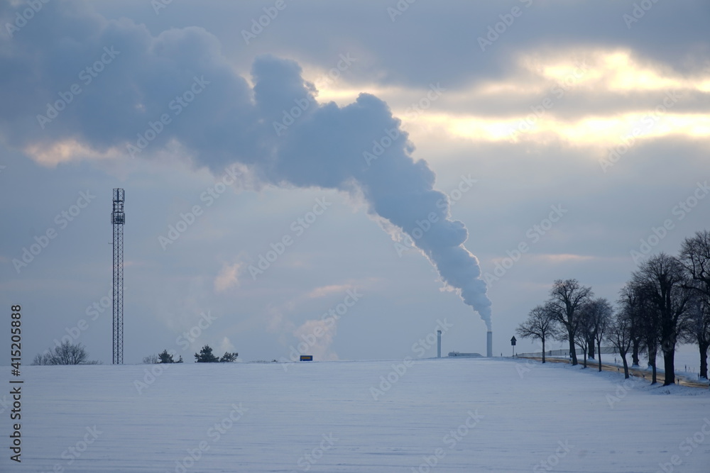 Winterlandschaft mit Industriestandort und Rauchschwaden aus dem Schornstein