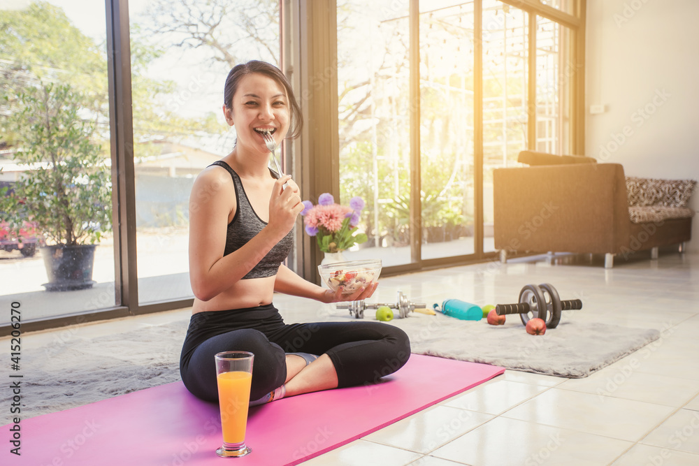 Healthy Asian woman smiling in sportswear eating salad fruit at home. Eating diet and exercise relaxation concept. Healthy Asian woman smiling in sportswear eating salad fruit at home. Eating diet and exercise relaxation concept.