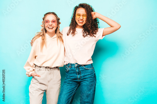 Two young beautiful smiling international hipster female in trendy summer clothes. Sexy carefree women posing near pink blue in studio. Positive models having fun. Concept of friendship