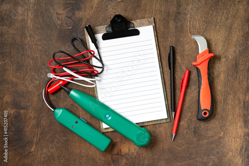 Tools of an electrician-installer or builder on a brown wooden table. Construction tools: wire stripper knife, cable tracker, notepad and pens on the table. Top view with copyspace
