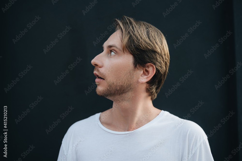 Side view portrait of a man wearing white t-shirt looking up at dark wall