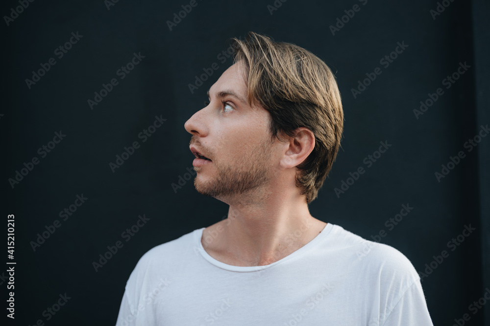 Side view portrait of a man wearing white t-shirt looking up at dark wall Side view portrait of a man wearing white t-shirt looking up at dark wall