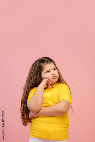 Offended. Happy, smiley little caucasian girl isolated on coral pink studio background with copyspace for ad. Looks happy, cheerful. Childhood, education, human emotions, facial expression concept.