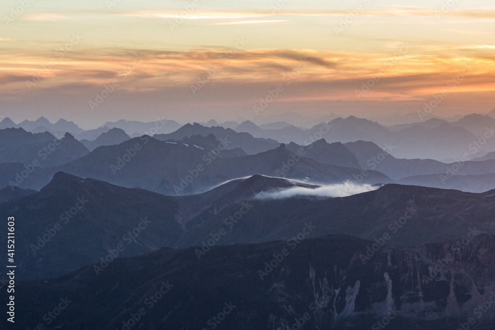 misty mountain ranges in a golden sunrise in the swiss alps