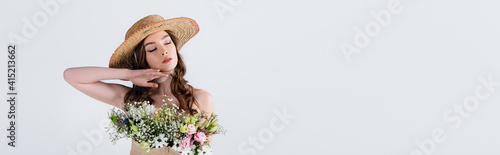 Young woman in stylish straw hat with flowers in blouse standing with closed eyes isolated on grey, banner