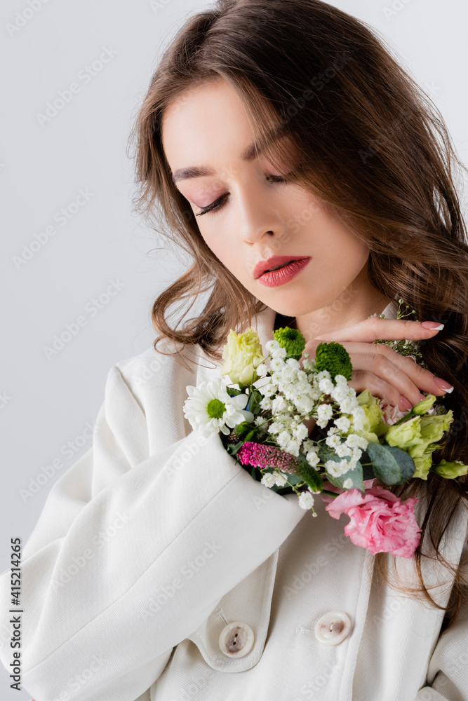 Young model in coat with flowers in sleeve standing isolated on grey