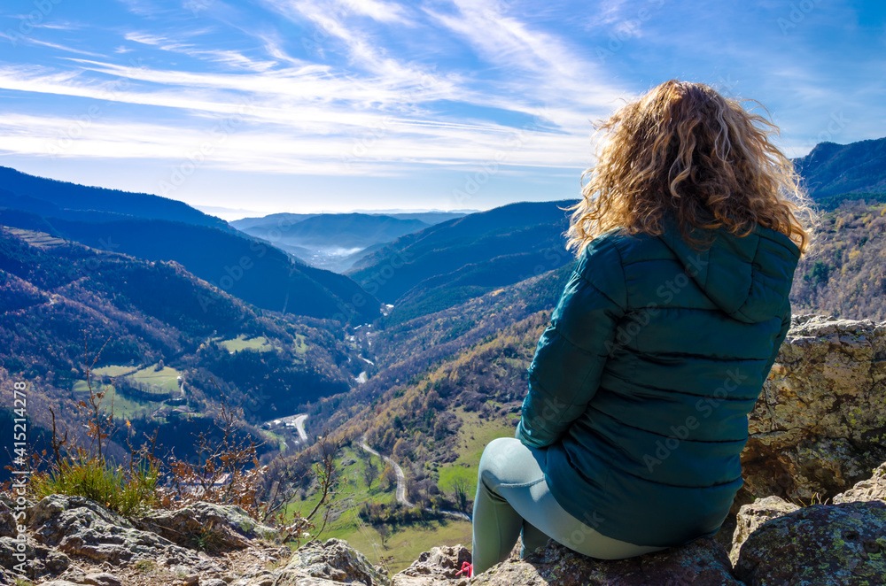 Naklejka premium Blond woman with curly hair, sitting on the mountain, looking at the fantastic views of the Ribes Valley, in the Ripolles region, Girona