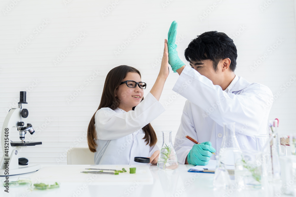 Adult Asian man and African American girl doing tests of plants in classroom. Group of diversity scientists learning science and doing analysis for germs and bacteria with microscope in the laboratory Adult Asian man and African American girl doing tests of plants in classroom. Group of diversity scientists learning science and doing analysis for germs and bacteria with microscope in the laboratory