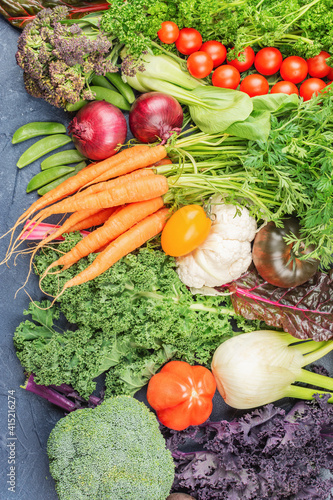 Assortment of organic vegetables broccoli cauliflower carrots tomatoes kale pak choy. Healthy local farm produce on blue concrete table, top view, selective focus