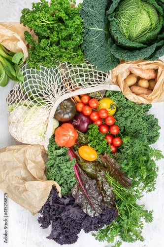 Eco organic shopping, colorful vegetables broccoli cauliflower carrots tomatoes kale pak choy chard in net and paper bags. Healthy local farm produce on white wooden table, top view, selective focus photo