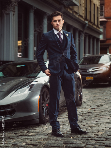 Young successful entrepreneur man standing near sport luxury car wearing a classic suit