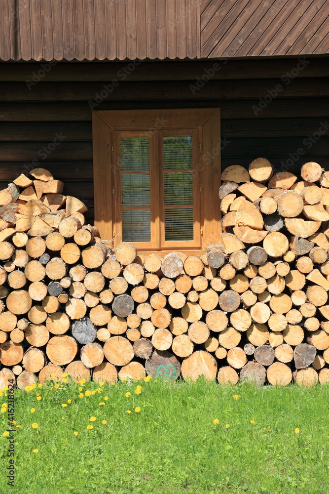 aufgeschlichtetes Brennholz vor einzelnem Fenster in Holzhaus aufgeschlichtetes Brennholz vor einzelnem Fenster in Holzhaus